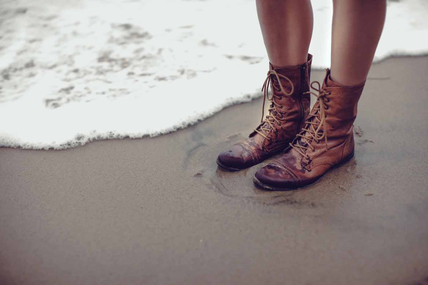 Brown lace-up boots at the edge of the surf on wet sand