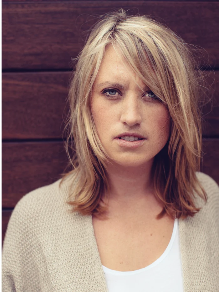A woman in a cream sweater against a dark red wall