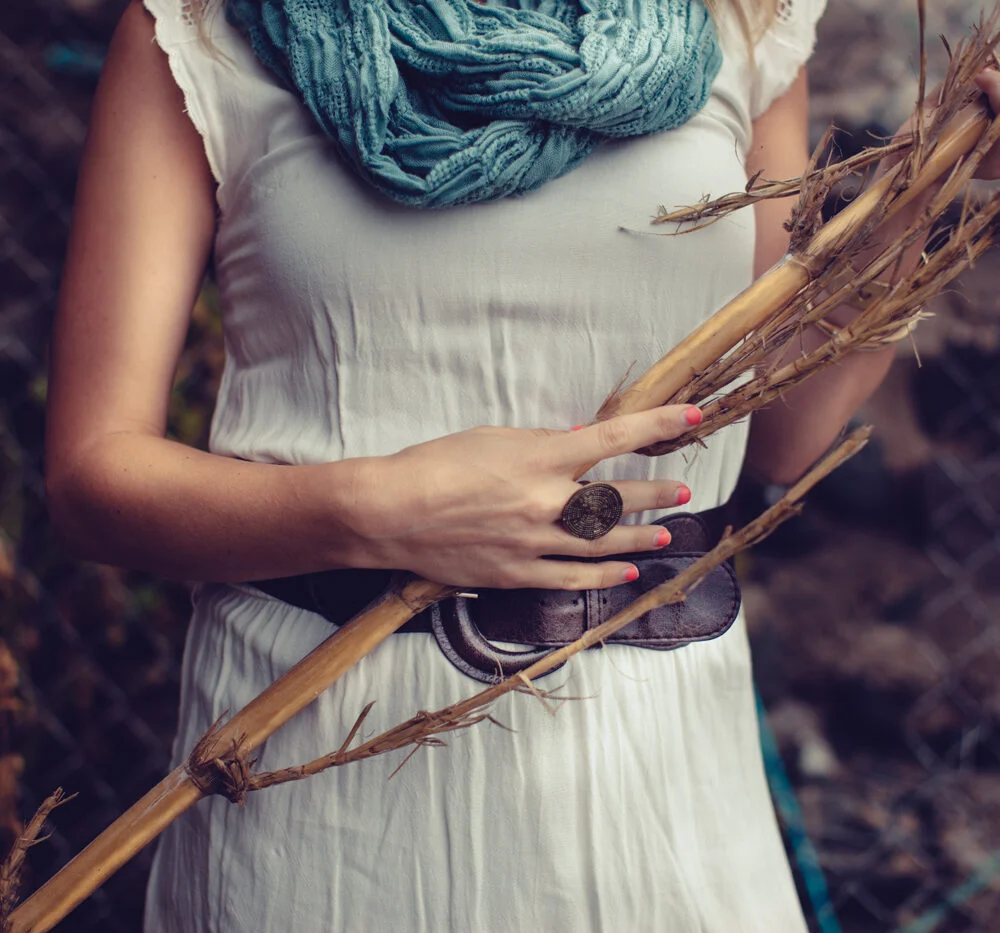 Hands holding a dry branch against a white dress and teal scarf