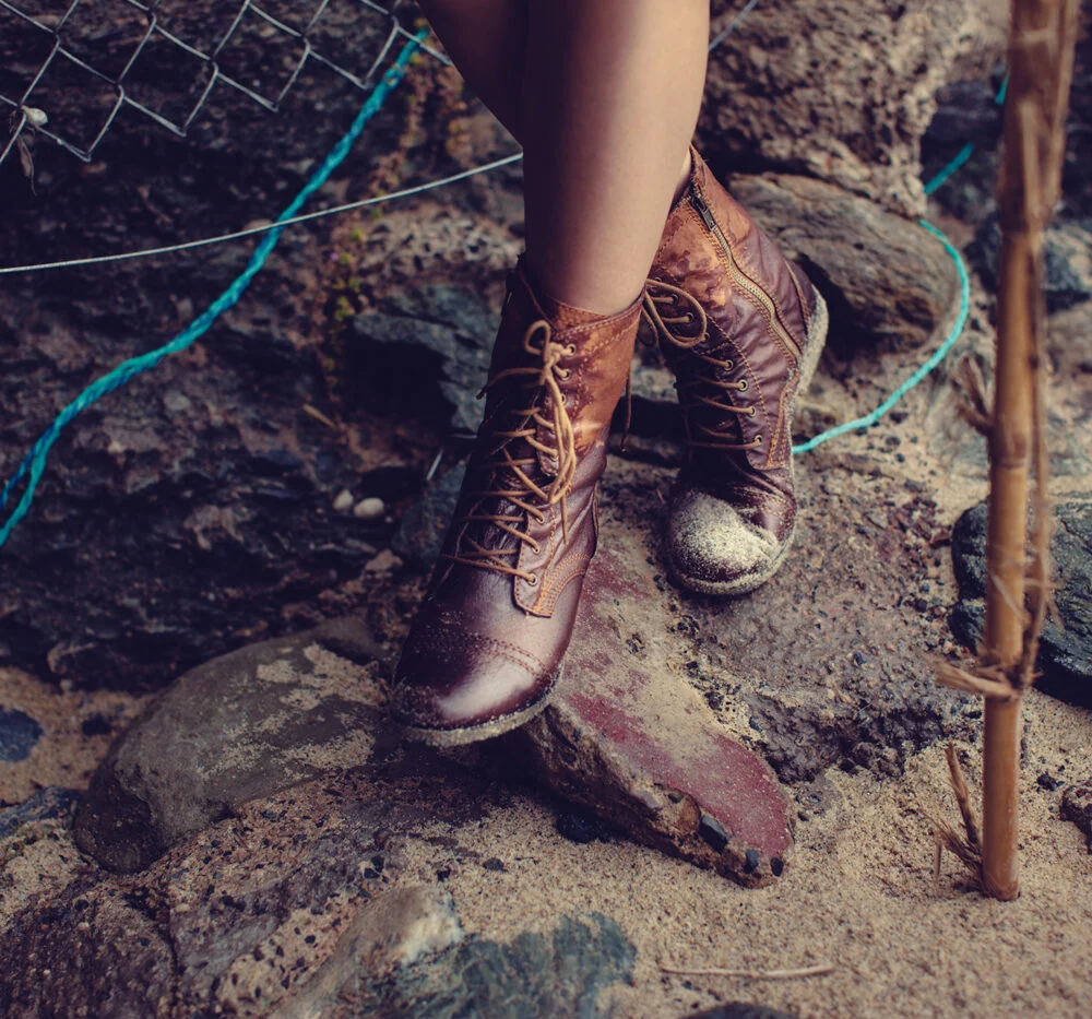 Lace-up boots on wet rocks beside a driftwood stick
