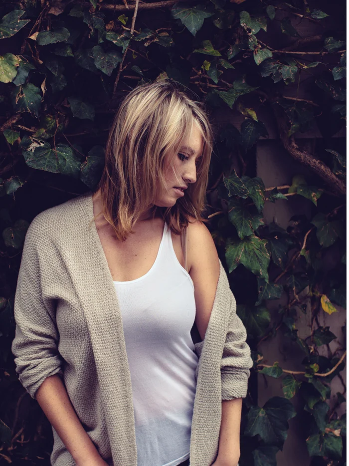 A woman in an oatmeal cardigan against ivy