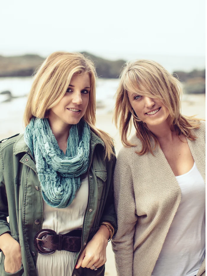 Two friends in sweaters and scarves on a gray beach