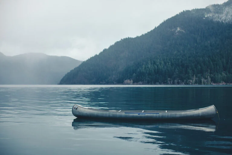 An empty canoe on still water under misty mountains at Lake Crescent