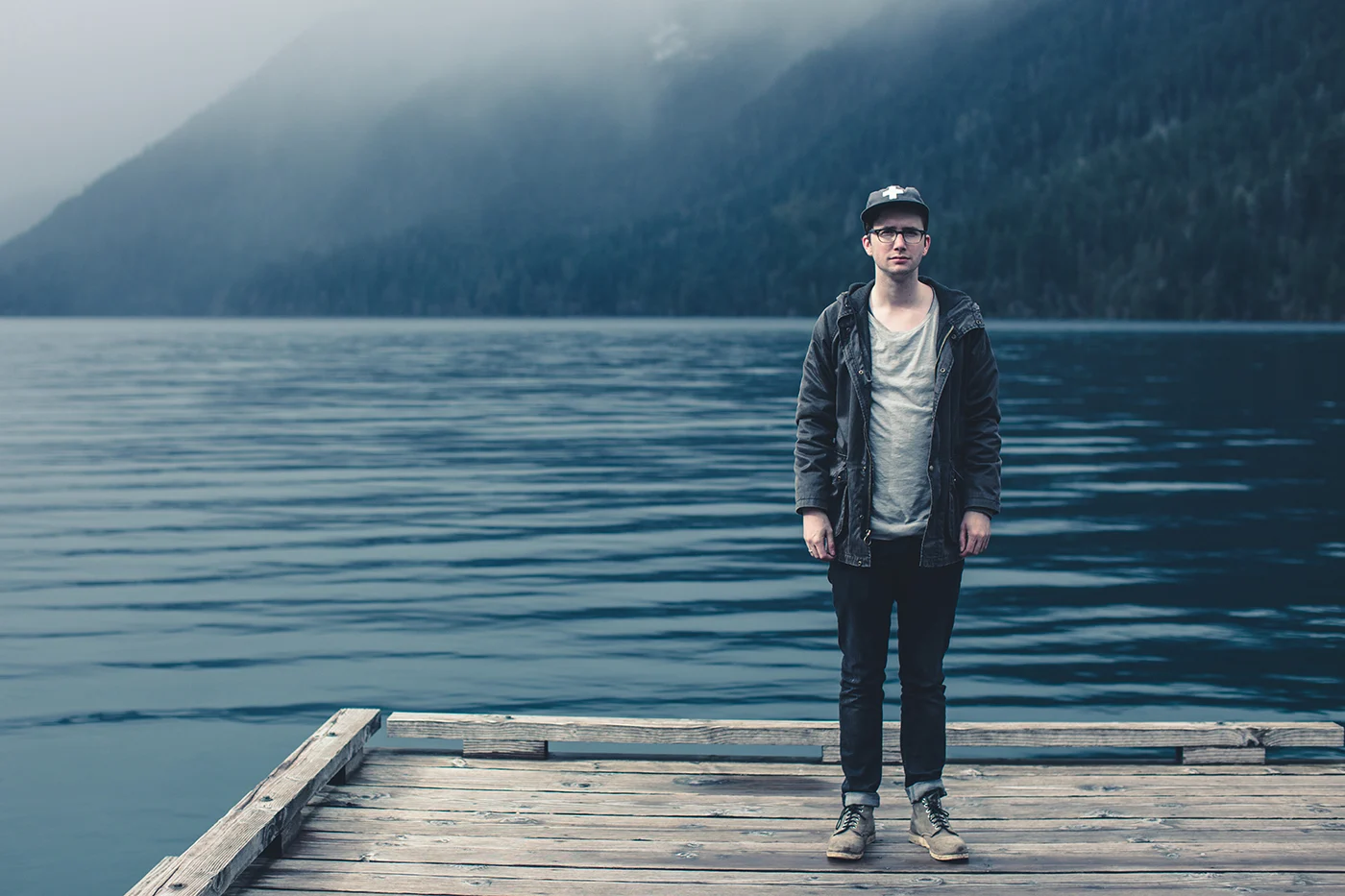A young man in a cap standing at the end of a wooden dock on Lake Crescent