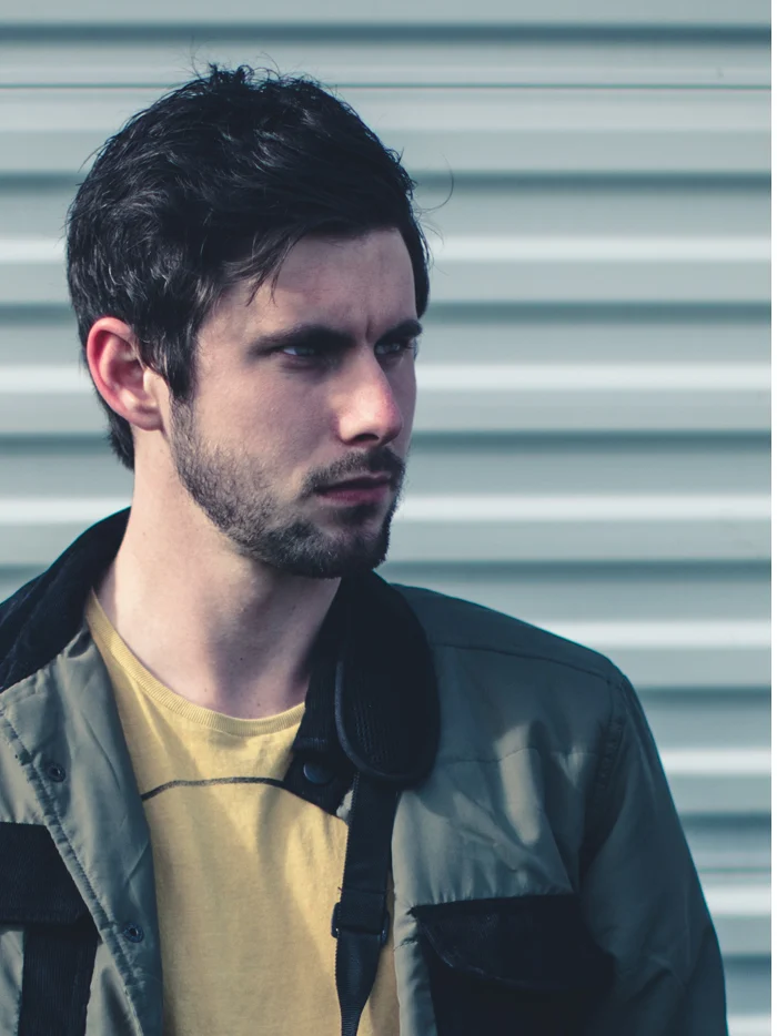 A man in a gray jacket against a corrugated metal wall