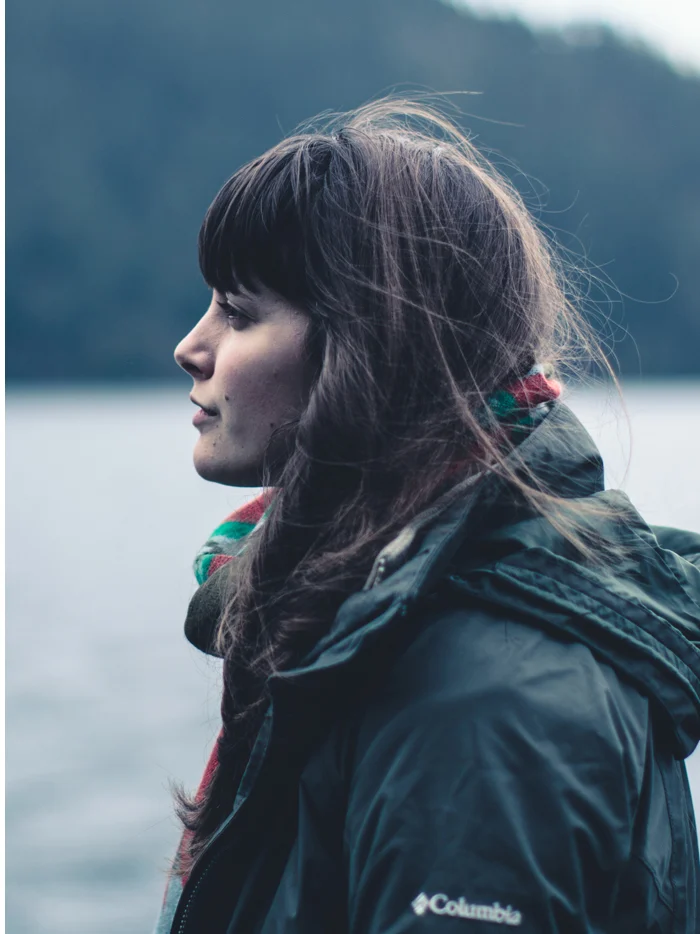 A woman in a rain jacket looking out over the lake in profile
