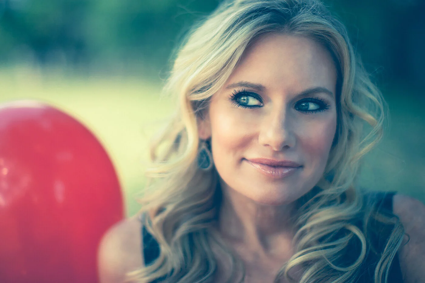 A close portrait of a blond woman beside a red balloon