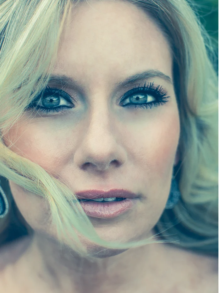A close portrait of a blond woman with her hair blowing across her face