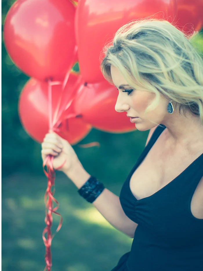 A woman in a black dress holding the strings of red balloons