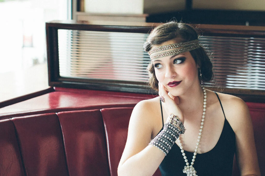 A woman in a beaded headband and pearls in a red diner booth