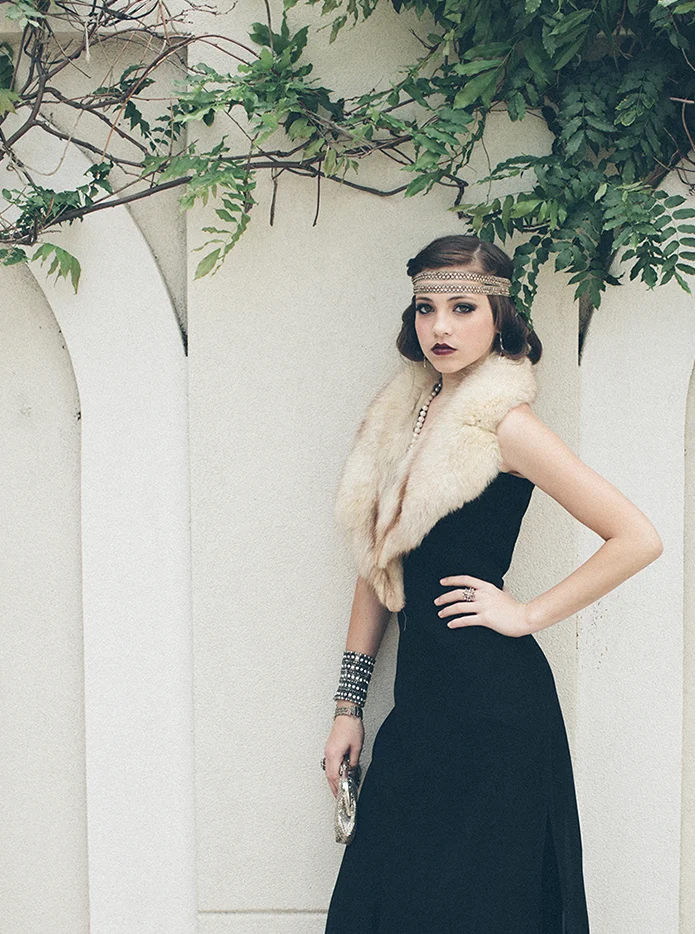 A woman in a long black dress and a fur stole under a garden arch