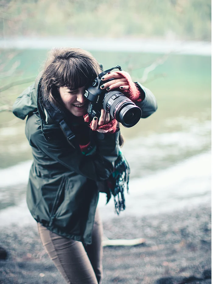 A photographer in a green jacket crouching on a pebble beach to take a picture